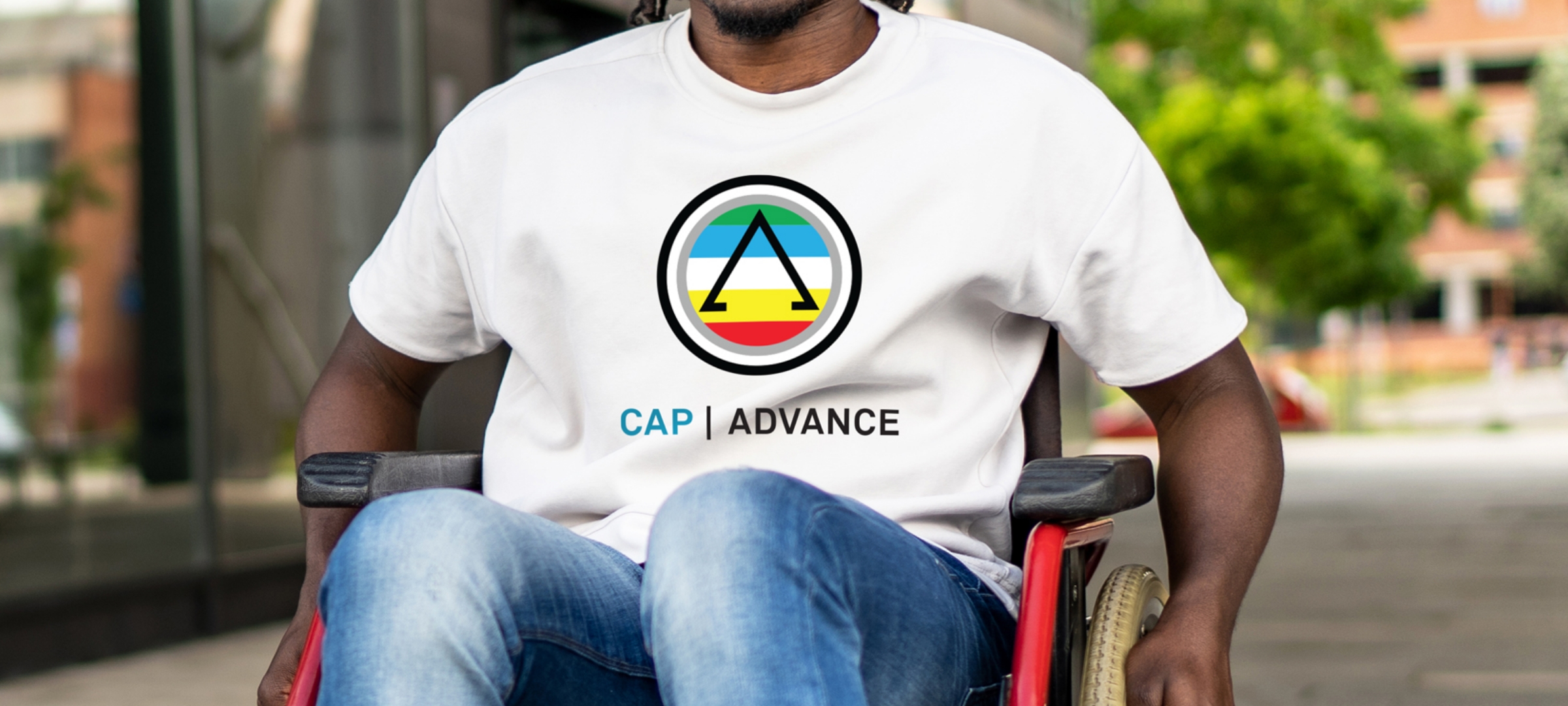 Person seated in a wheelchair wearing a white T-shirt with the CAP Advance logo outdoors.