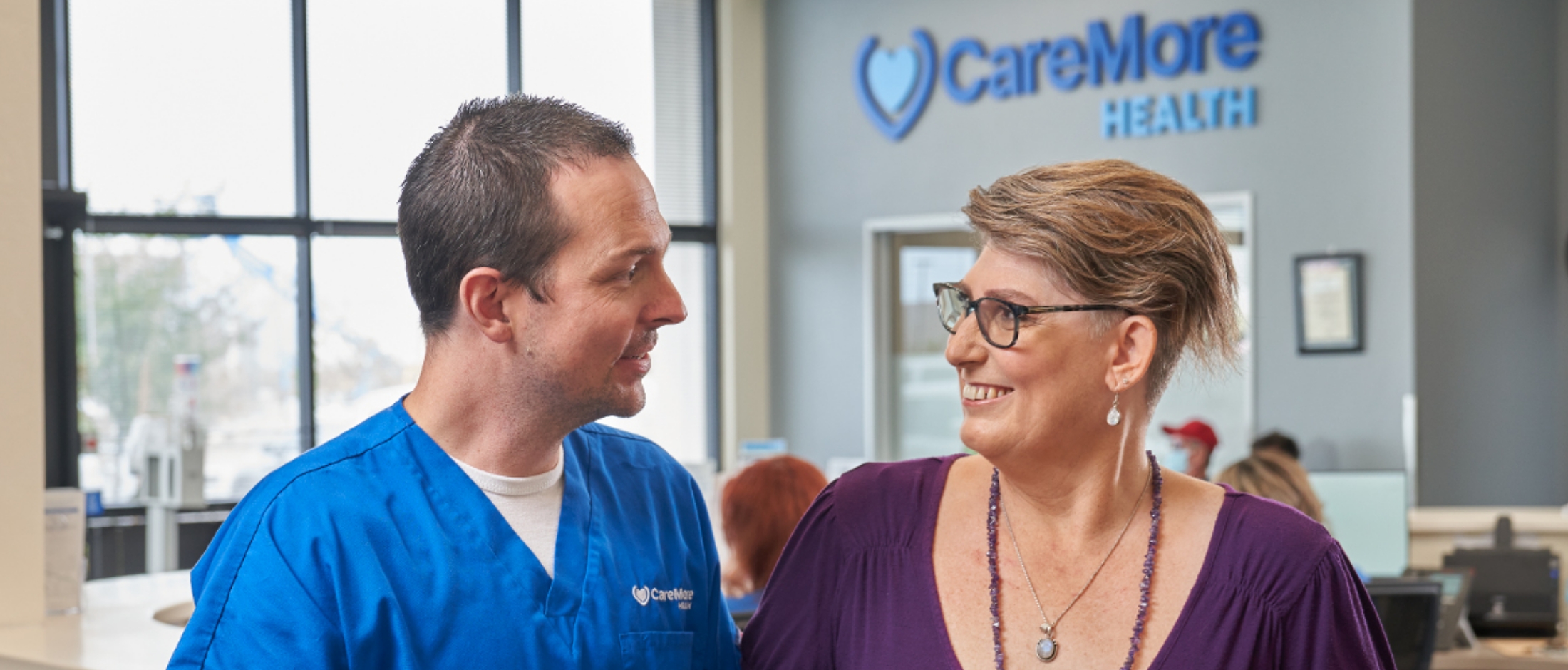 A CareMore patient and healthcare provider smile inside a CareMore office.